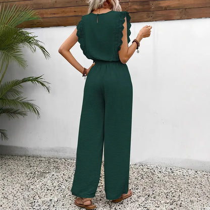 Woman wearing a green jumpsuit standing against a white wall with a wooden top.