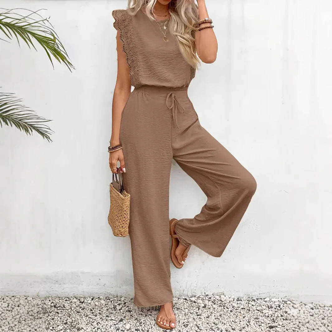 Woman wearing a brown jumpsuit holding a straw bag against a white wall.
