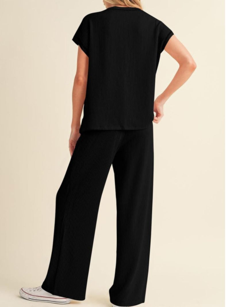 Person wearing a black outfit with wide-leg pants on a beige background