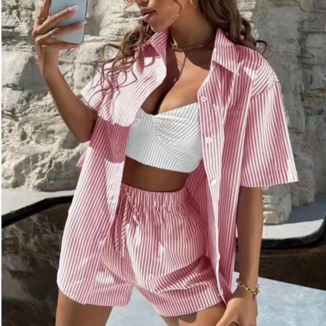 Woman wearing a pink and white striped outfit taking a selfie against a stone wall.